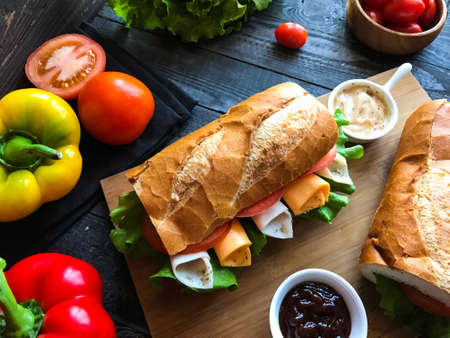 Delicious and Tasty sandwiches with turkey, ham, cheese, tomatoes and salad over a wooden table full of fresh vegetables.の写真素材