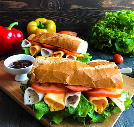 Delicious and Tasty sandwiches with turkey, ham, cheese, tomatoes and salad over a wooden table full of fresh vegetables.の写真素材