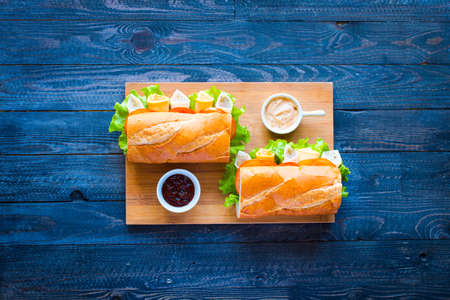 Delicious and Tasty sandwiches with turkey, ham, cheese, tomatoes and salad over a wooden table full of fresh vegetables.の写真素材