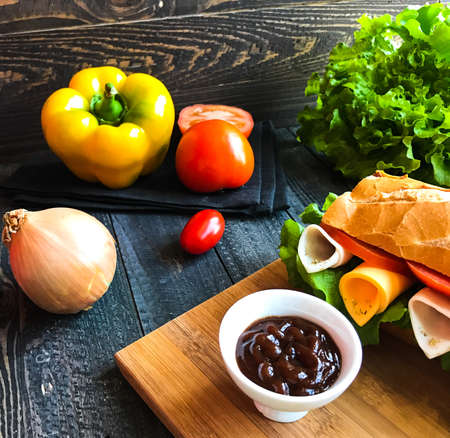 Delicious and Tasty sandwiches with turkey, ham, cheese, tomatoes and salad over a wooden table full of fresh vegetables.の写真素材