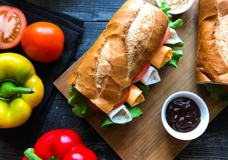 Delicious and Tasty sandwiches with turkey, ham, cheese, tomatoes and salad over a wooden table full of fresh vegetables.の写真素材