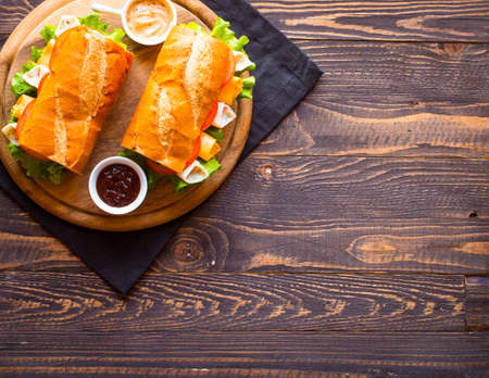 Delicious and Tasty sandwiches with turkey, ham, cheese, tomatoes and salad over a wooden table full of fresh vegetables.の写真素材