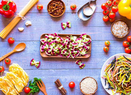Pasta background with vegetables and herbs on a wooden table. Free space for text. Top viewの写真素材