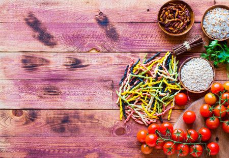 Pasta background with vegetables and herbs on a wooden table. Free space for text. Top viewの写真素材