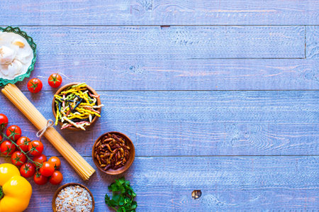 Pasta background with vegetables and herbs on a wooden table. Free space for text. Top view