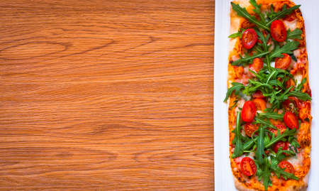 Home maid fresh pizza with tomatoes, rucola and mozzarella cheese over a wooden background. Top view.の写真素材