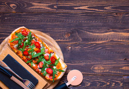 Home maid fresh pizza with tomatoes, rucola and mozzarella cheese over a wooden background. Top view.の写真素材