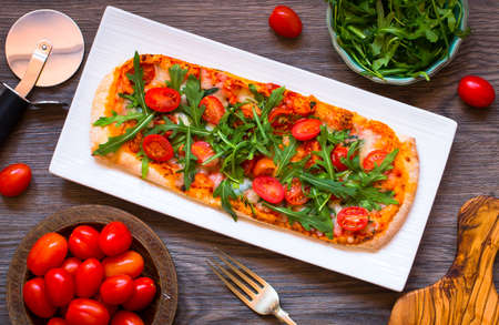 Home maid fresh pizza with tomatoes, rucola and mozzarella cheese over a wooden background. Top view.の写真素材