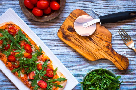 Home maid fresh pizza with tomatoes, rucola and mozzarella cheese over a wooden background. Top view.の写真素材