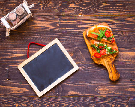 Home maid fresh pizza with tomatoes, rucola and mozzarella cheese over a wooden background. Top view.の写真素材