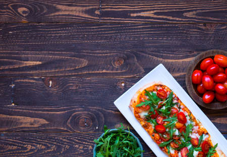 Home maid fresh pizza with tomatoes, rucola and mozzarella cheese over a wooden background. Top view.の写真素材