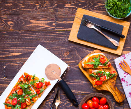 Home maid fresh pizza with tomatoes, rucola and mozzarella cheese over a wooden background. Top view.の写真素材