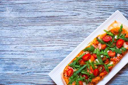 Home maid fresh pizza with tomatoes, rucola and mozzarella cheese over a wooden background. Top view.の写真素材