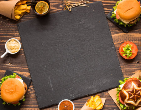 Top view of delicious hamburger, with vegetables and fries, on a wooden background.