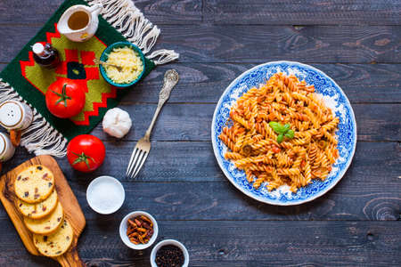Fusilli pasta with tomato sauce, tomatoes, onion, garlic, dried paprika, olives, pepper and olive oil, on a wooden background. Top viewの写真素材