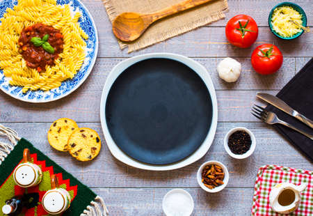 Fusilli pasta with tomato sauce, tomatoes, onion, garlic, dried paprika, olives, pepper and olive oil, on a wooden background. Top viewの写真素材