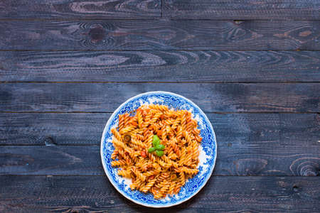 Fusilli pasta with tomato sauce, tomatoes, onion, garlic, dried paprika, olives, pepper and olive oil, on a wooden background. Top viewの写真素材