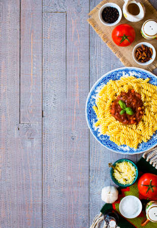 Fusilli pasta with tomato sauce, tomatoes, onion, garlic, dried paprika, olives, pepper and olive oil, on a wooden background. Top viewの写真素材