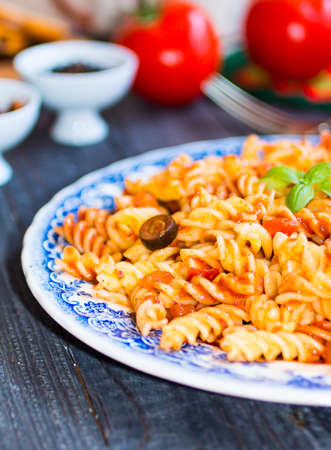 Fusilli pasta with tomato sauce, tomatoes, onion, garlic, dried paprika, olives, pepper and olive oil, on a wooden background. Top viewの写真素材