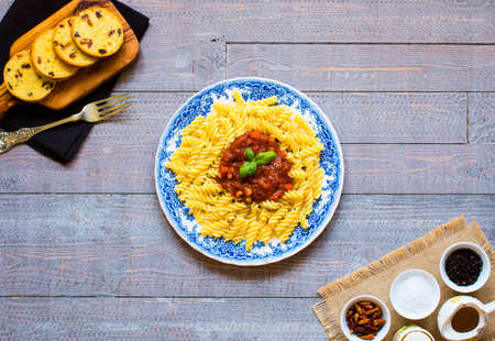 Fusilli pasta with tomato sauce, tomatoes, onion, garlic, dried paprika, olives, pepper and olive oil, on a wooden background. Top viewの写真素材