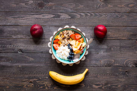 Healthy breakfast, cereal with yogurt, strawberries, blueberry, apple, banana, on wooden rustic background. Top viewの写真素材