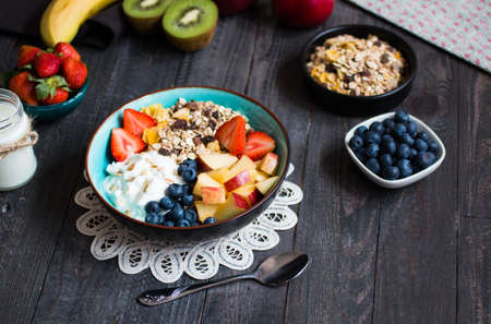 Healthy breakfast, cereal with yogurt, strawberries, blueberry, apple, banana, on wooden rustic background. Top viewの写真素材