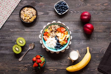 Healthy breakfast, cereal with yogurt, strawberries, blueberry, apple, banana, on wooden rustic background. Top viewの写真素材