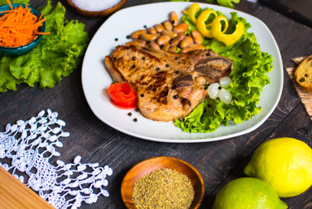 Pork steak homemade cooking with spices leaves lettuce on wooden cutting board, and a dish, on a...