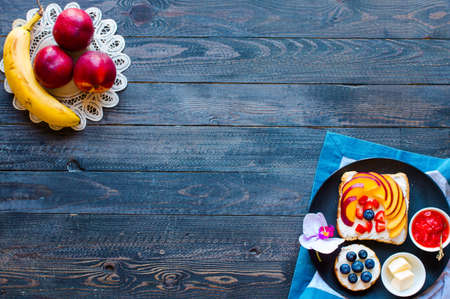 Delicious healthy breakfast, fruit sandwiches with different fillings, cheese, banana, strawberry, fishing, butter, blueberry, on a different wooden background. top viewの写真素材