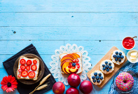 Delicious healthy breakfast, fruit sandwiches with different fillings, cheese, banana, strawberry, fishing, butter, blueberry, on a different wooden background. top viewの写真素材