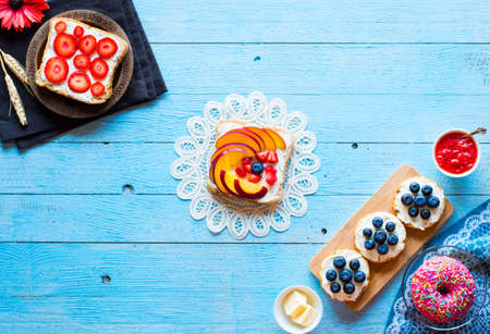 Delicious healthy breakfast, fruit sandwiches with different fillings, cheese, banana, strawberry, fishing, butter, blueberry, on a different wooden background. top viewの写真素材