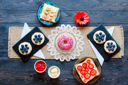 Delicious healthy breakfast, fruit sandwiches with different fillings, cheese, banana, strawberry, fishing, butter, blueberry, on a different wooden background. top viewの写真素材