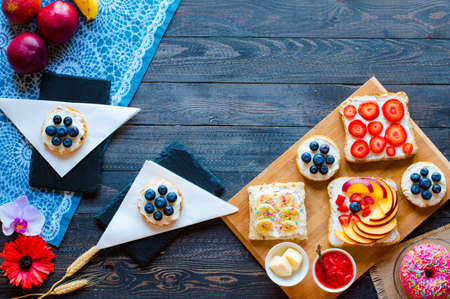 Delicious healthy breakfast, fruit sandwiches with different fillings, cheese, banana, strawberry, fishing, butter, blueberry, on a different wooden background. top viewの写真素材