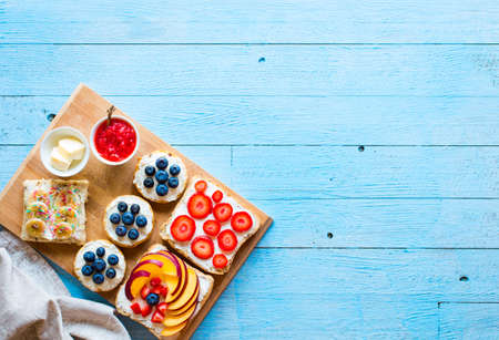 Delicious healthy breakfast, fruit sandwiches with different fillings, cheese, banana, strawberry, fishing, butter, blueberry, on a different wooden background. top viewの写真素材