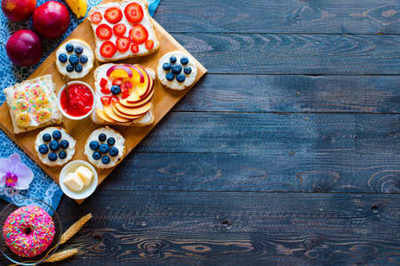 Delicious healthy breakfast, fruit sandwiches with different fillings, cheese, banana, strawberry, fishing, butter, blueberry, on a different wooden background. top viewの写真素材