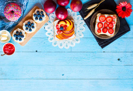 Delicious healthy breakfast, fruit sandwiches with different fillings, cheese, banana, strawberry, fishing, butter, blueberry, on a different wooden background. top viewの写真素材