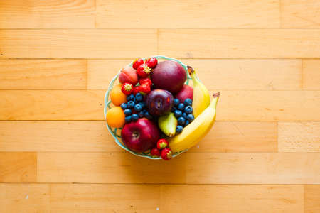 Bowl of fresh fruit with banana, apple, strawberries, apricots, blueberries, plums, whole grains, forks, spoon, free space for text. top viewの写真素材