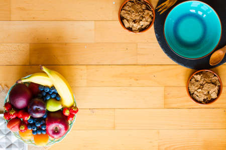 Bowl of fresh fruit with banana, apple, strawberries, apricots, blueberries, plums, whole grains, forks, spoon, free space for text. top viewの写真素材