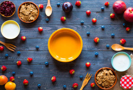 Bowl of fresh fruit with banana, apple, strawberries, apricots, blueberries, plums, whole grains, forks, spoon, free space for text. top viewの写真素材