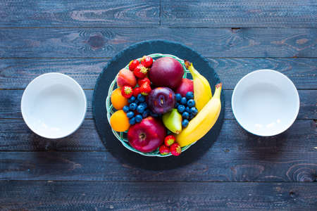 Bowl of fresh fruit with banana, apple, strawberries, apricots, blueberries, plums, whole grains, forks, spoon, free space for text. top viewの写真素材