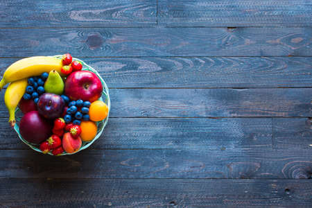 Bowl of fresh fruit with banana, apple, strawberries, apricots, blueberries, plums, whole grains, forks, spoon, free space for text. top viewの写真素材