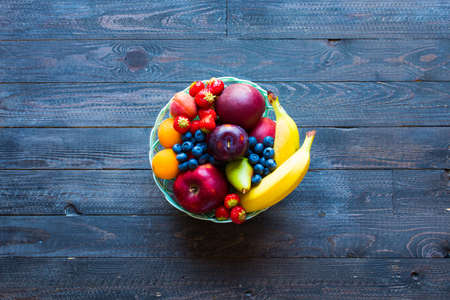 Bowl of fresh fruit with banana, apple, strawberries, apricots, blueberries, plums, whole grains, forks, spoon, free space for text. top viewの写真素材