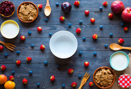 Bowl of fresh fruit with banana, apple, strawberries, apricots, blueberries, plums, whole grains, forks, spoon, free space for text. top viewの写真素材