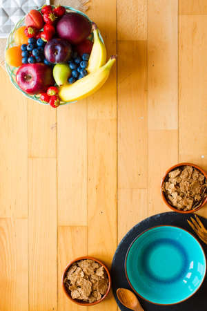 Bowl of fresh fruit with banana, apple, strawberries, apricots, blueberries, plums, whole grains, forks, spoon, free space for text. top viewの写真素材