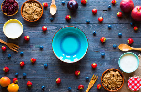 Bowl of fresh fruit with banana, apple, strawberries, apricots, blueberries, plums, whole grains, forks, spoon, free space for text. top viewの写真素材