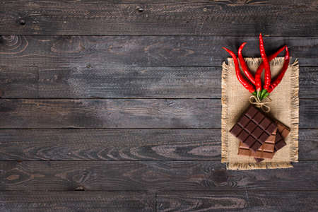Dark chocolate and milk chocolate, with red hot chili peppers, on a wooden background, free space for textの写真素材