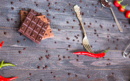 Dark chocolate and milk chocolate, with red hot chili peppers, on a wooden background, free space for textの写真素材