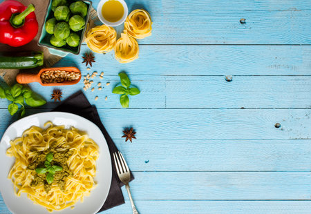 Pasta tagliatelle with pesto sauce and other vegetables on a wood background, free space for text....