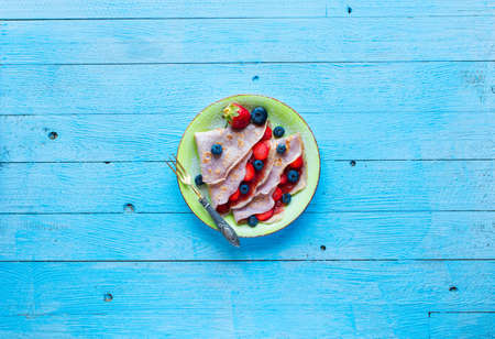 Fresh homemade crepes served on a plate with strawberries and blueberries, on a light blue wooden background, free space for text. Top viewの写真素材