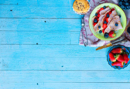 Fresh homemade crepes served on a plate with strawberries and blueberries, on a light blue wooden background, free space for text. Top viewの写真素材